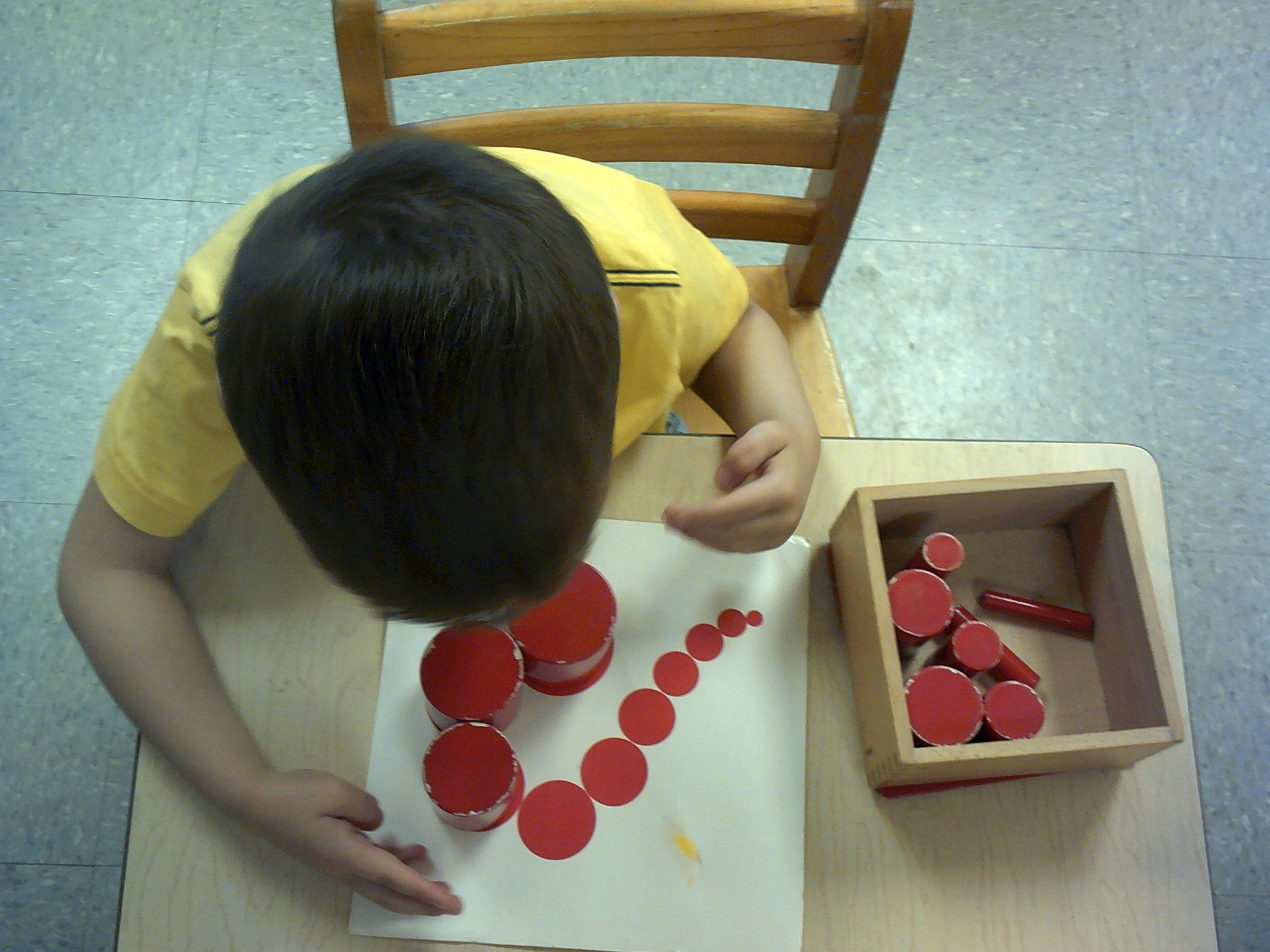 Child arranging red circular objects on a paper