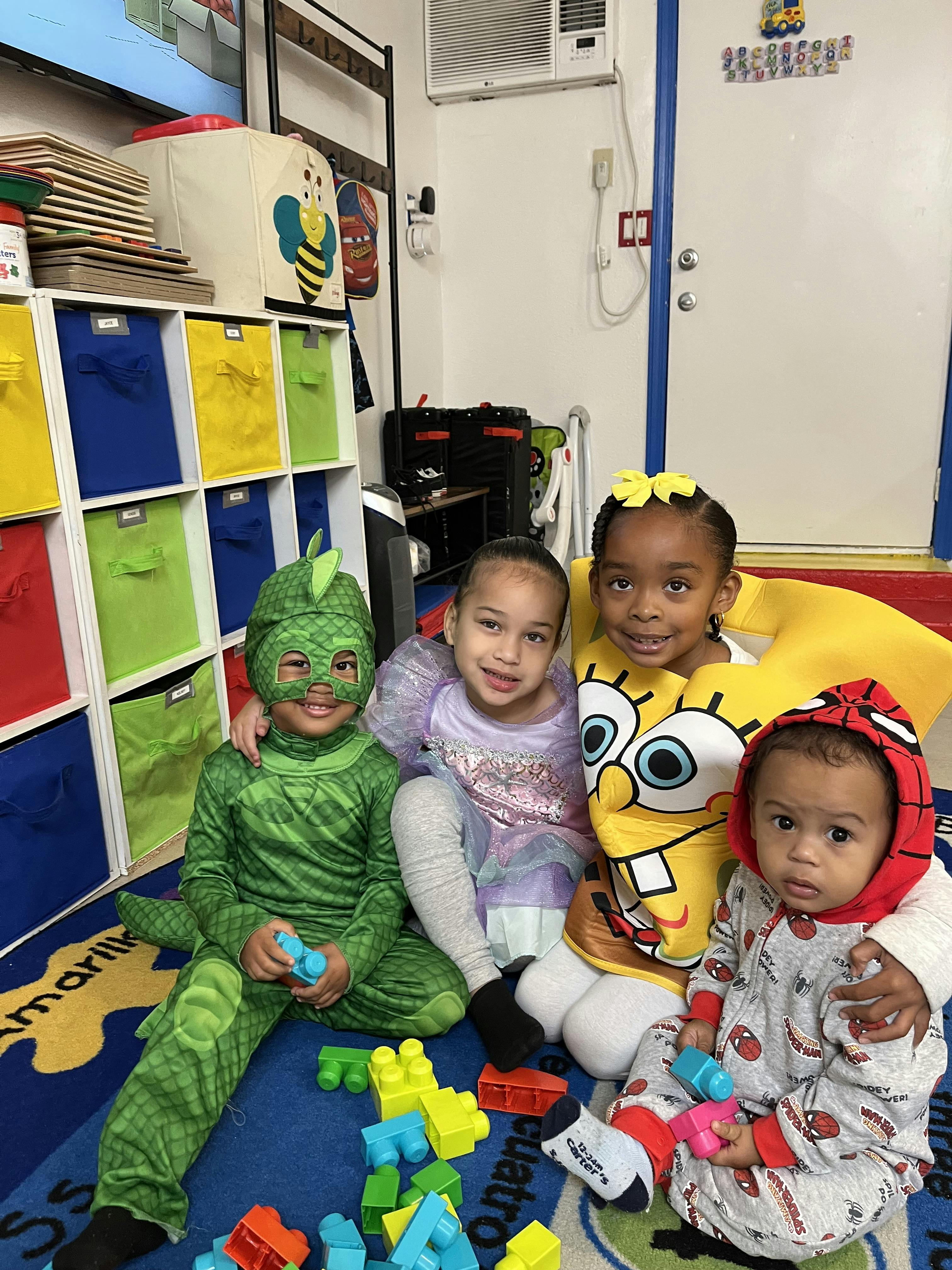 Four children in costumes sitting on a rug with building blocks