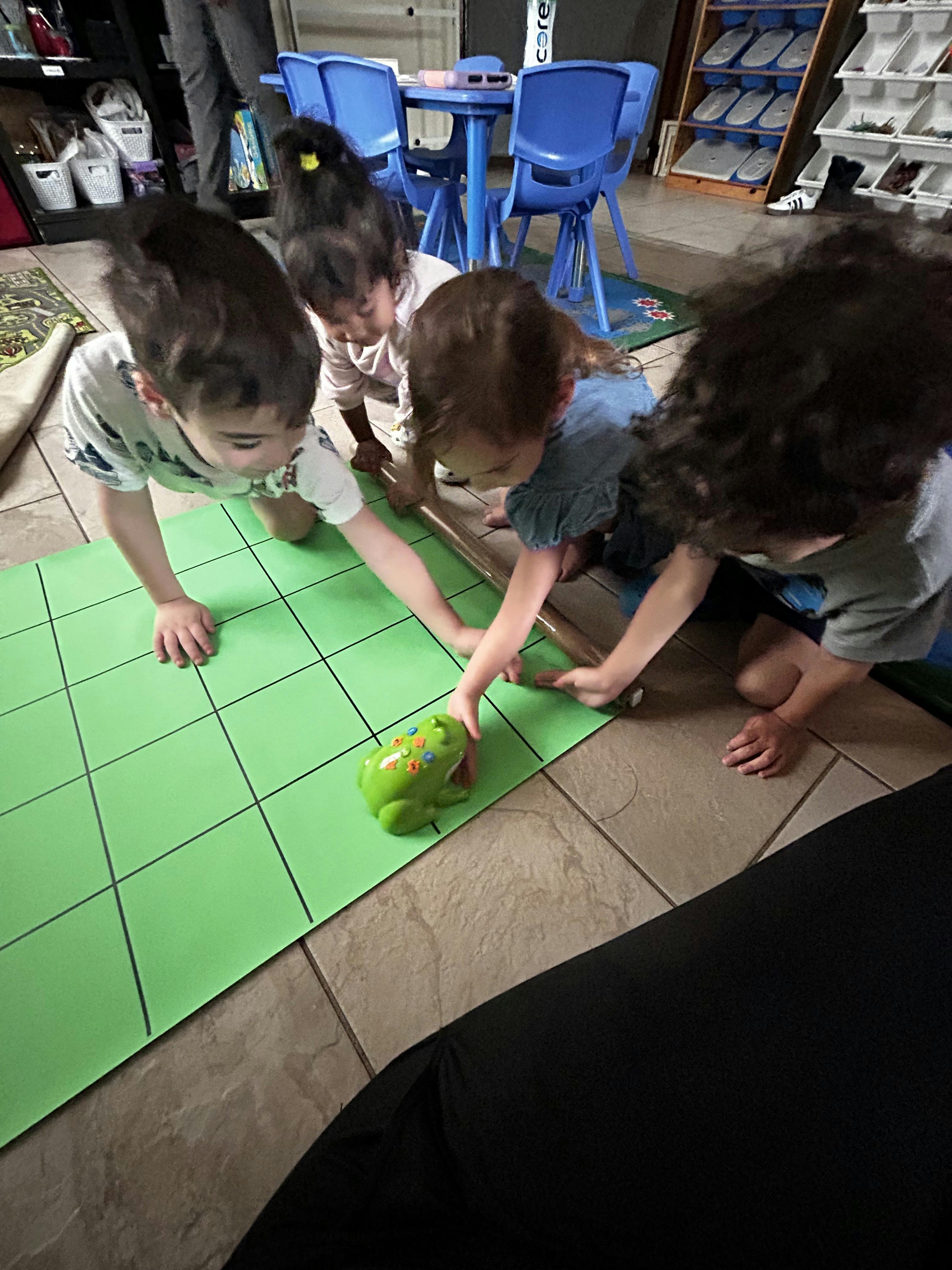 Four children playing with a small toy on a grid mat in a room