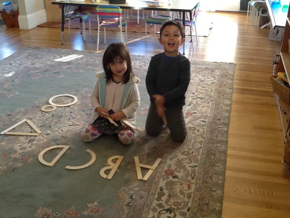 Two children kneeling on a rug with wooden letters and shapes