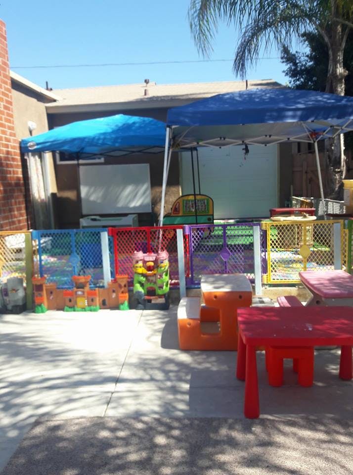 Outdoor play area with colorful fence, play structures, and small tables under canopies