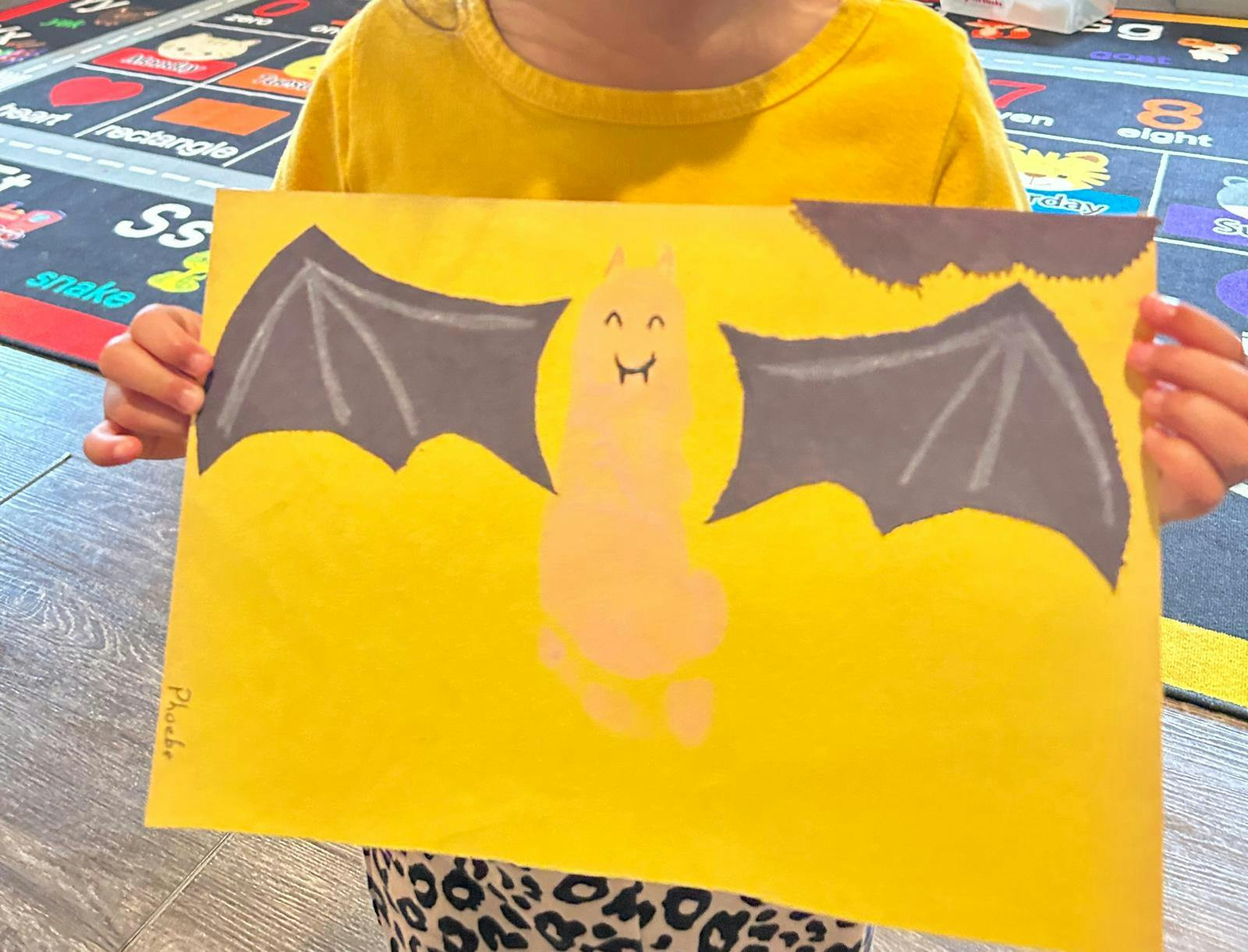 Child holding up a drawing of a bat with a footprint body made from a footprint