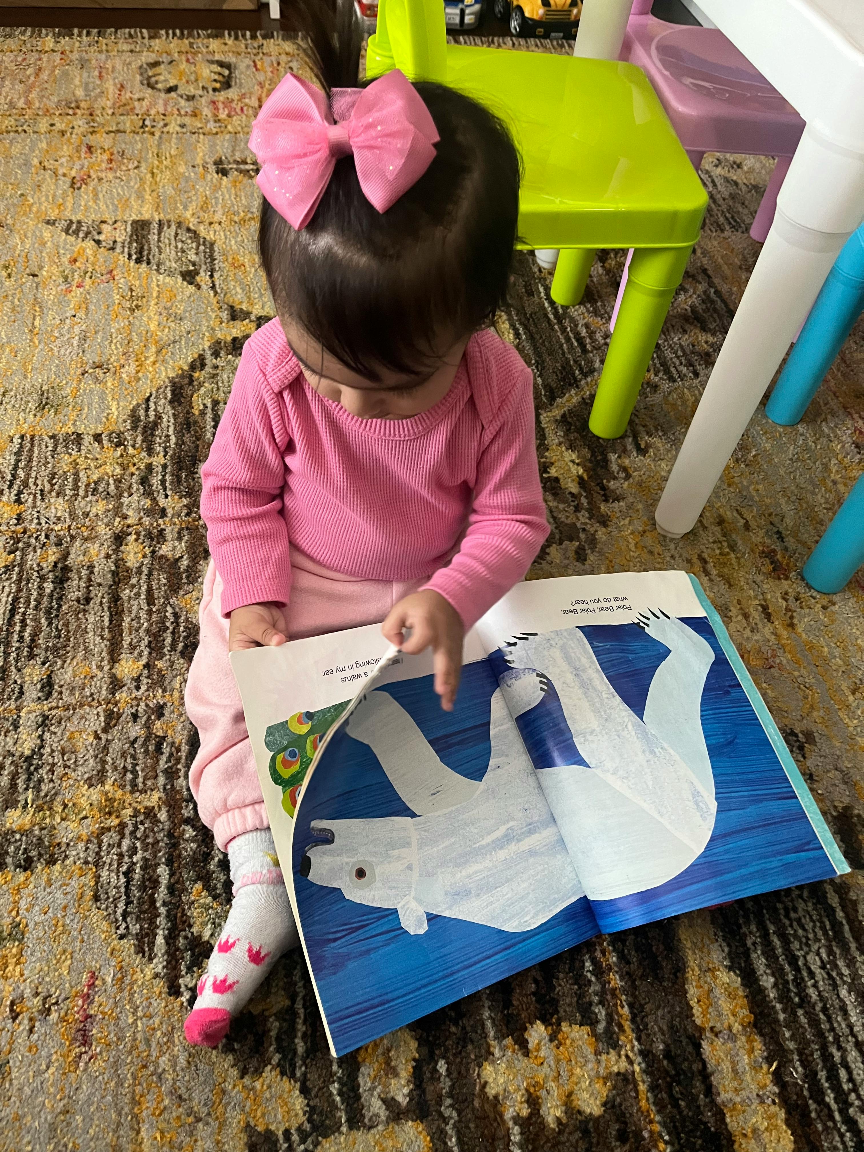Child with pink bow reading a book with a polar bear illustration