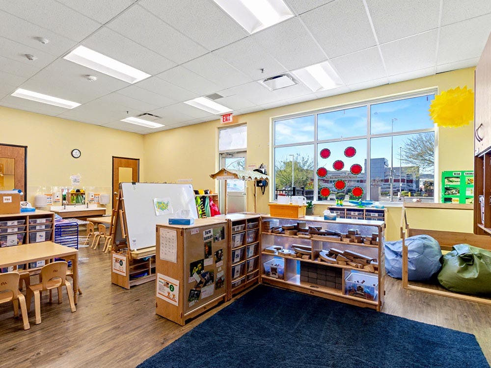 Empty classroom with small tables and chairs, whiteboards, and storage shelves