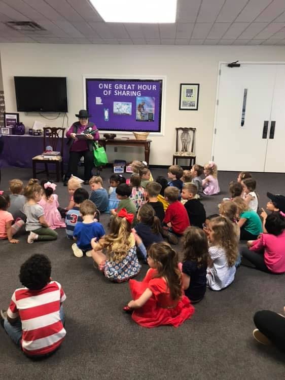 Person in a hat reading to a group of children sitting on the floor