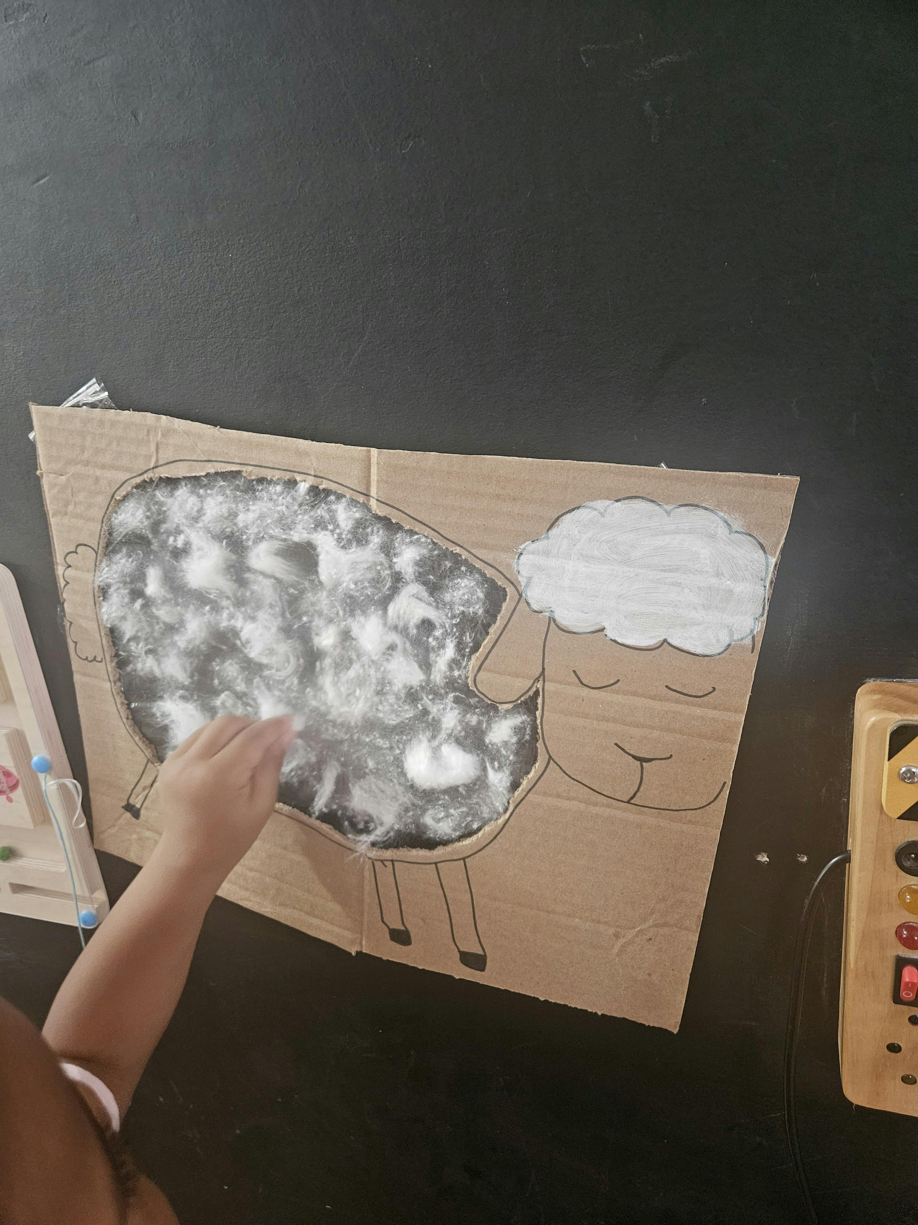 Child gluing cotton wool onto a cardboard cutout of a sheep