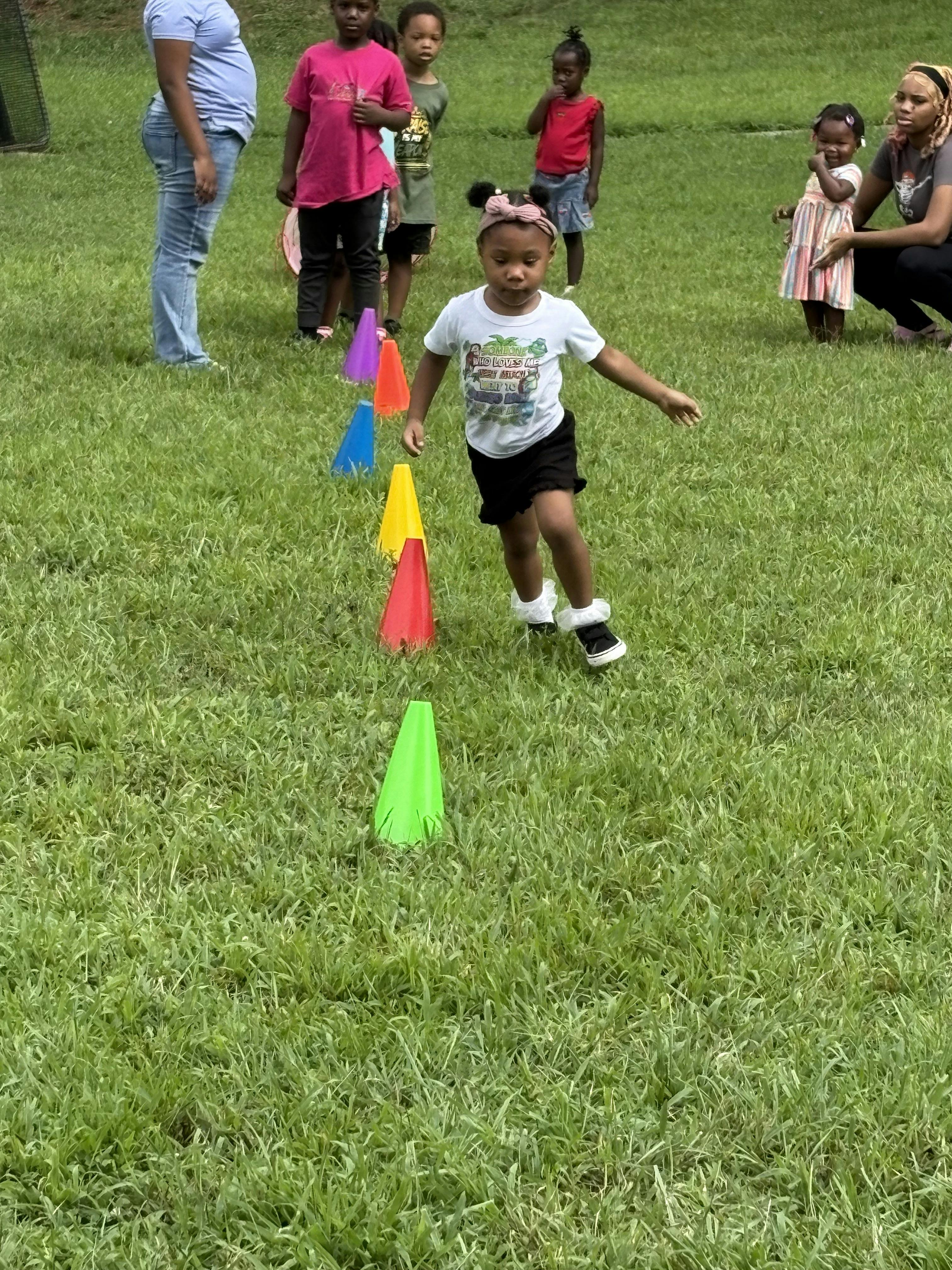 Child running past a row of colorful plastic cones on a grassy field