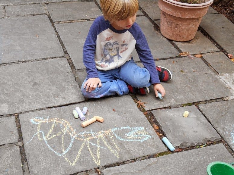 Child sitting on pavement drawing with chalk