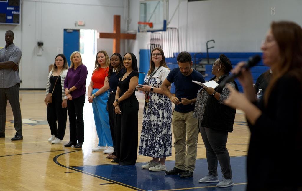 Group of people standing in a line on a basketball court, one person speaking into a microphone