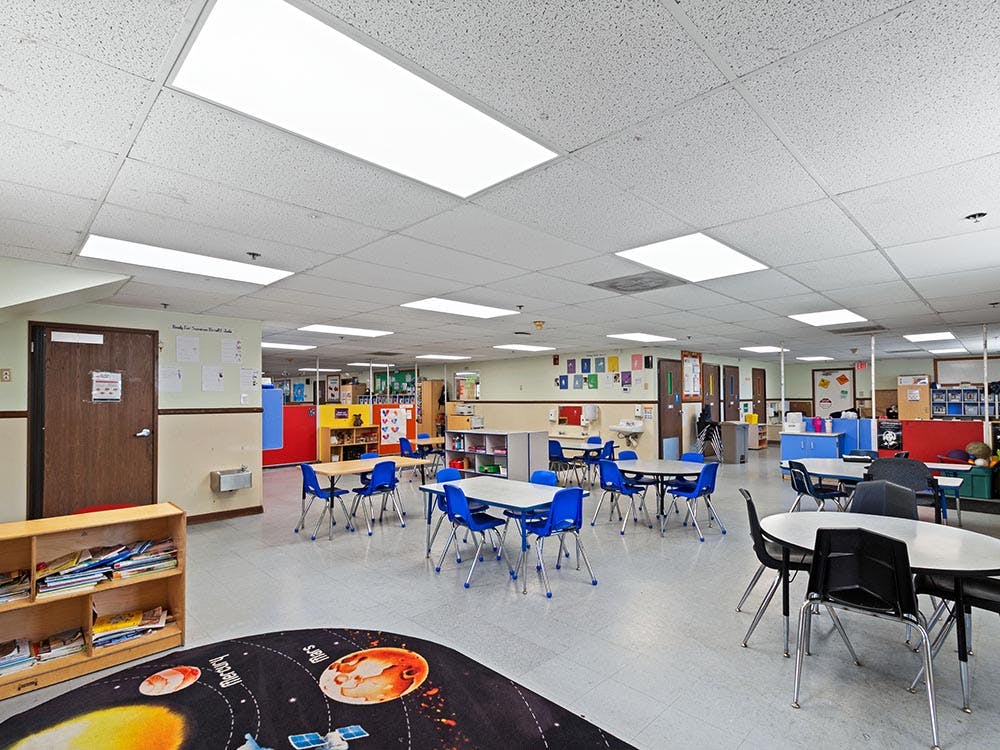 An empty classroom with multiple tables and chairs, and a space-themed rug