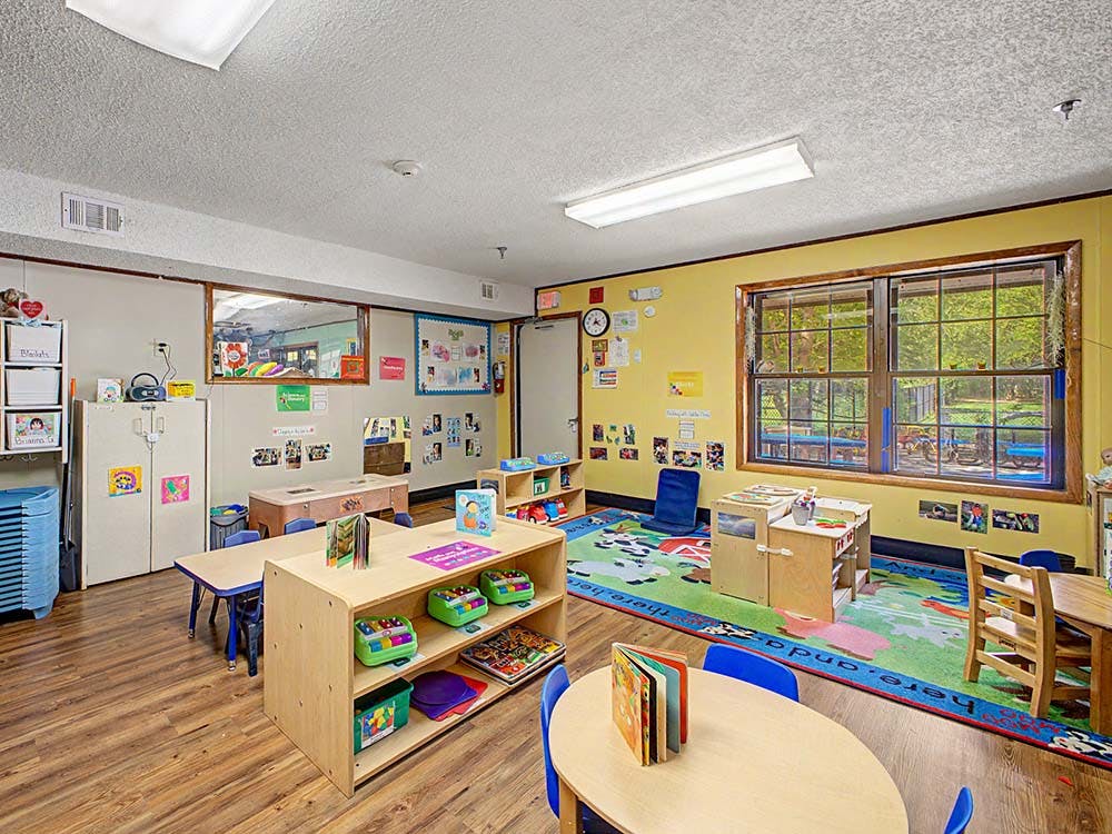 Colorful classroom with small tables, chairs, bookshelves, and a patterned rug