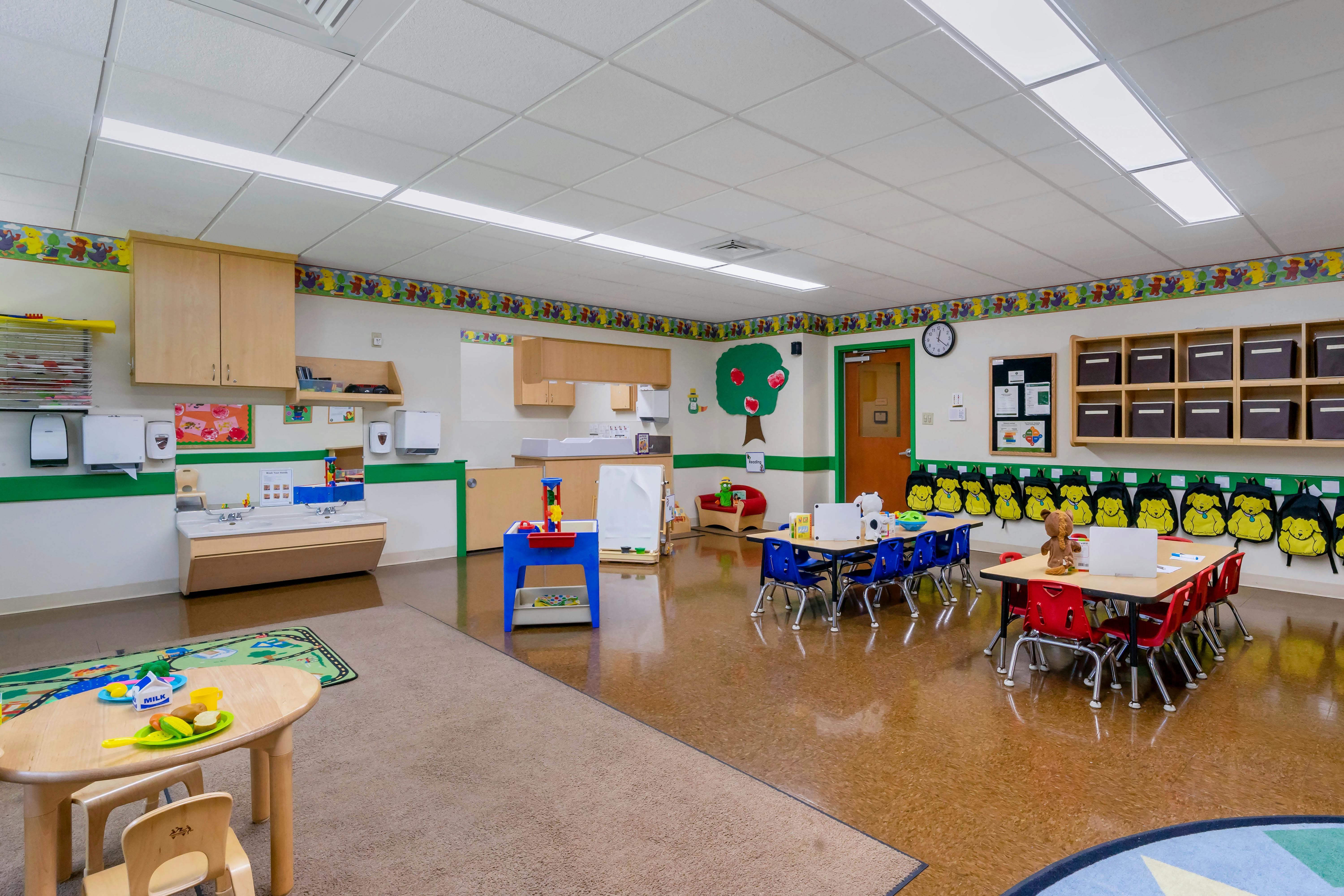Classroom with small tables and chairs, a sink area, and cubbies
