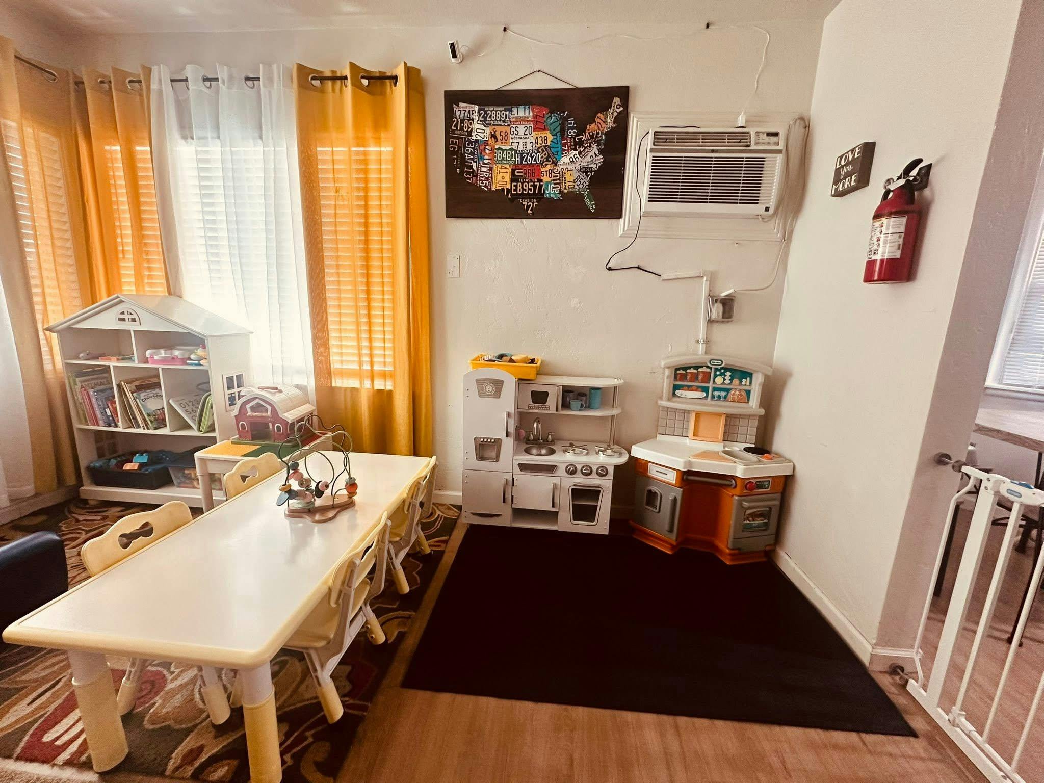 Children's play area with a long table, play kitchen, and toy shelf