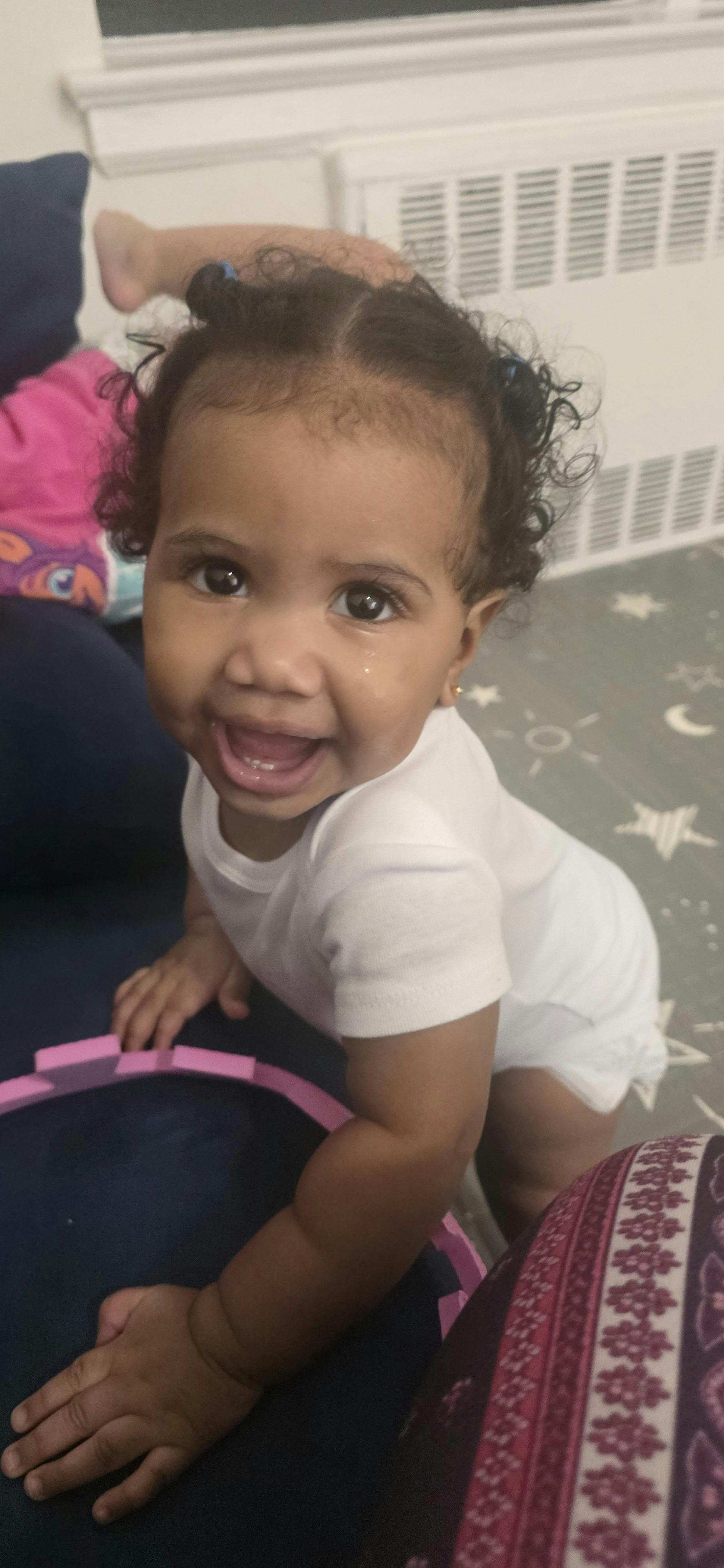 A toddler in a white onesie looking up