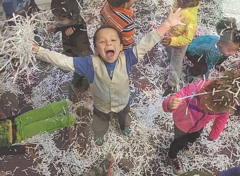 Child with arms outstretched among other children and shredded paper