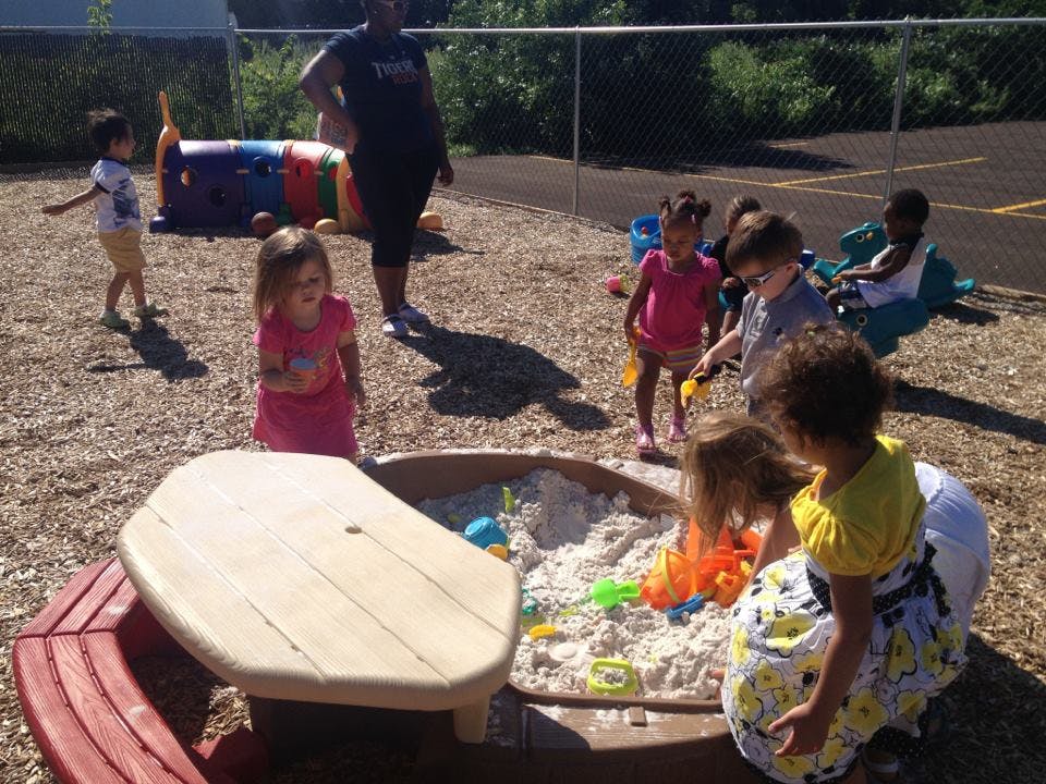 Children playing in a sandbox with a person supervising