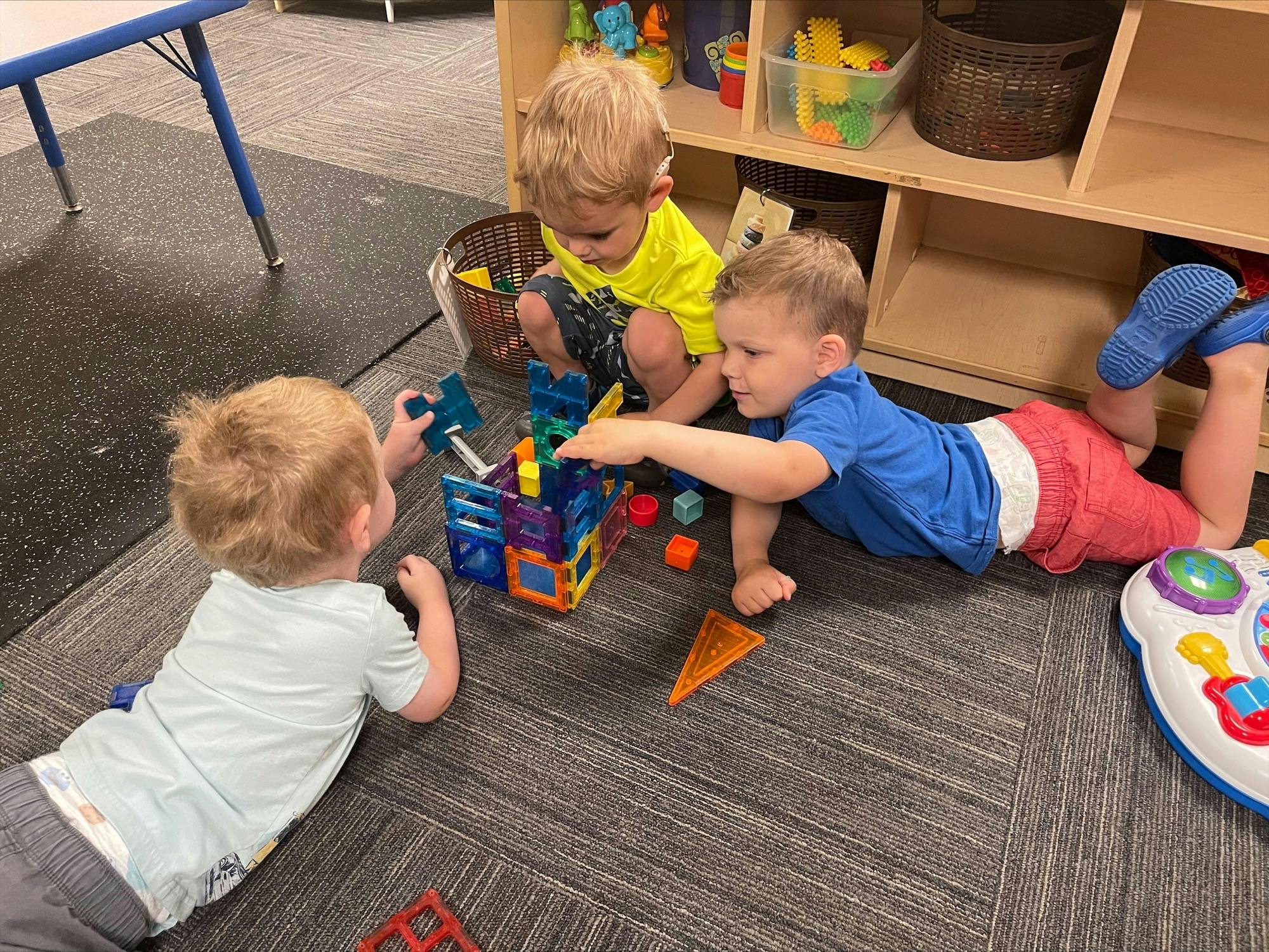 Three children playing with colorful building blocks on the floor