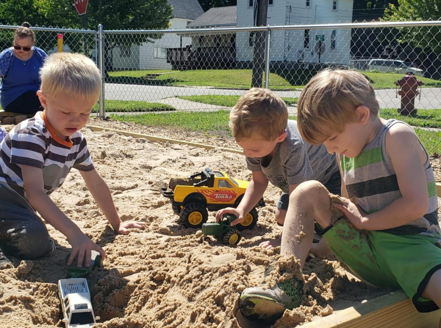 Three children playing with toy trucks in a sandbox