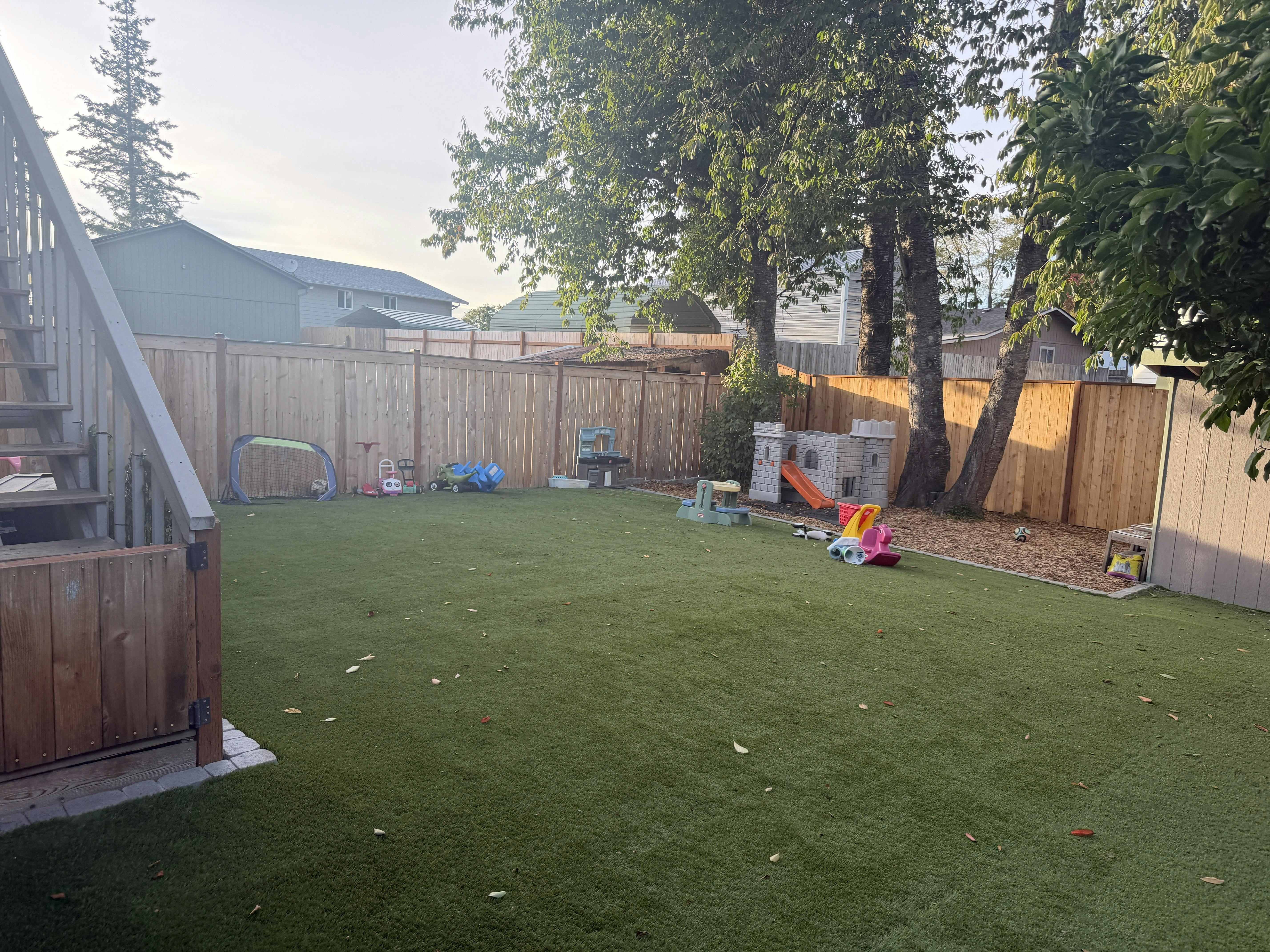 Childrens play equipment in a fenced backyard with artificial turf