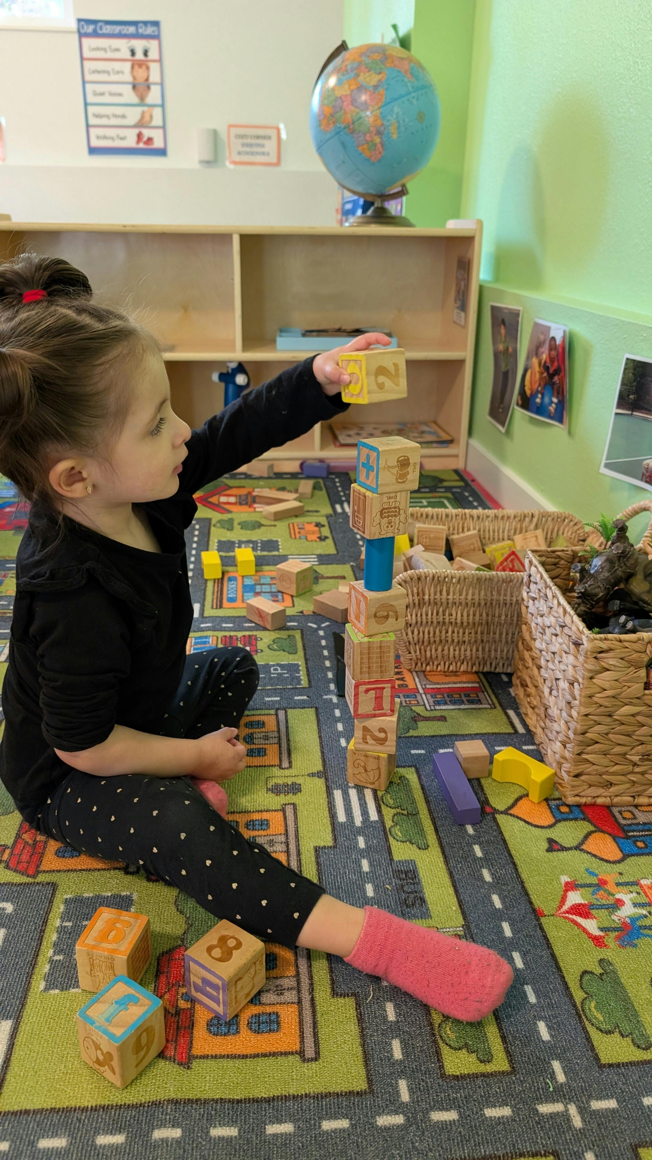 Child on floor stacking wooden blocks in a classroom