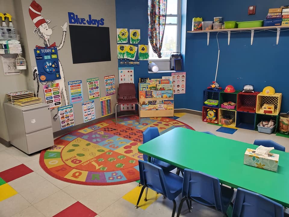 A colorful classroom with a green table and chairs, and a circular rug