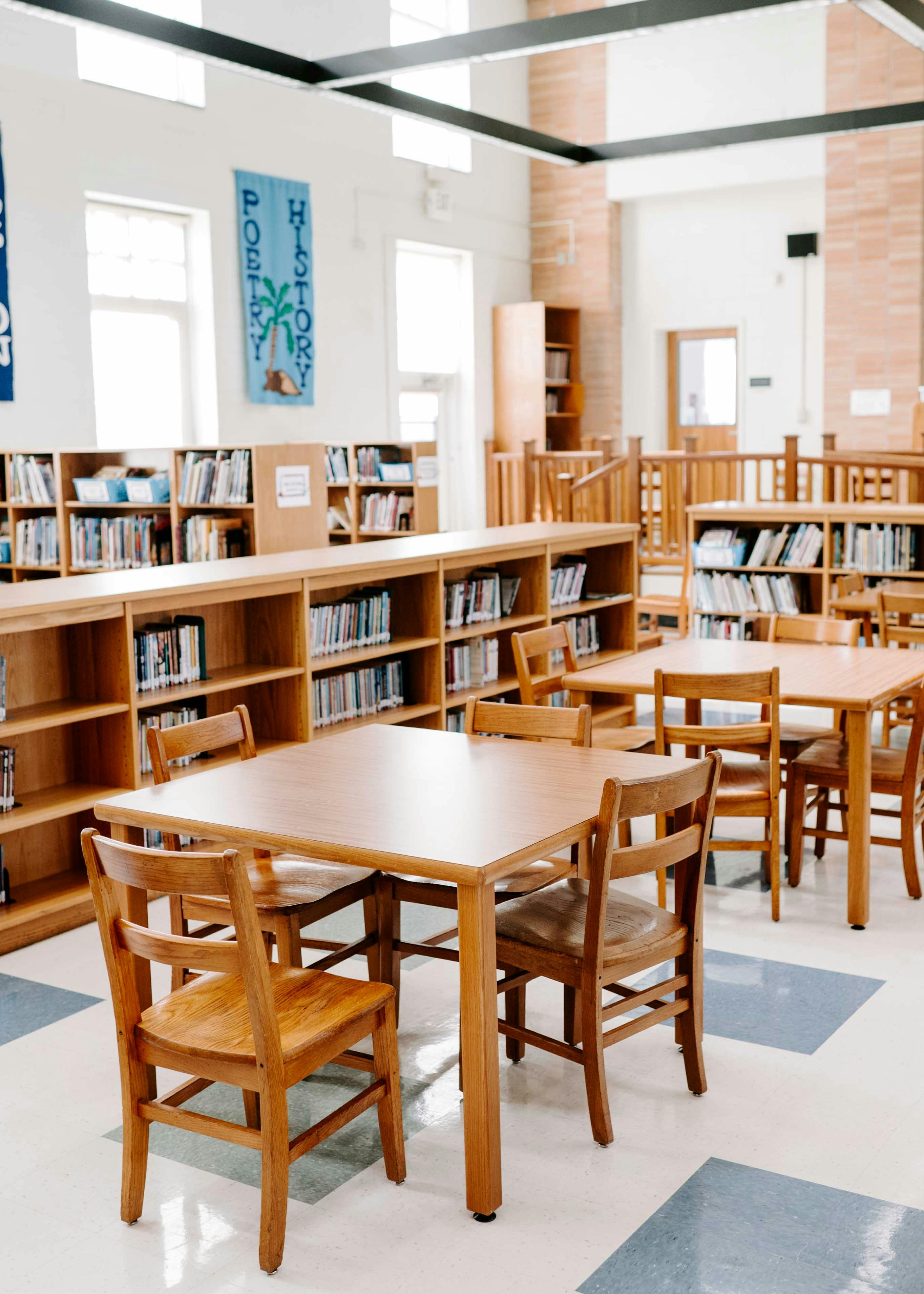 Empty library with wooden tables and chairs, bookshelves filled with books