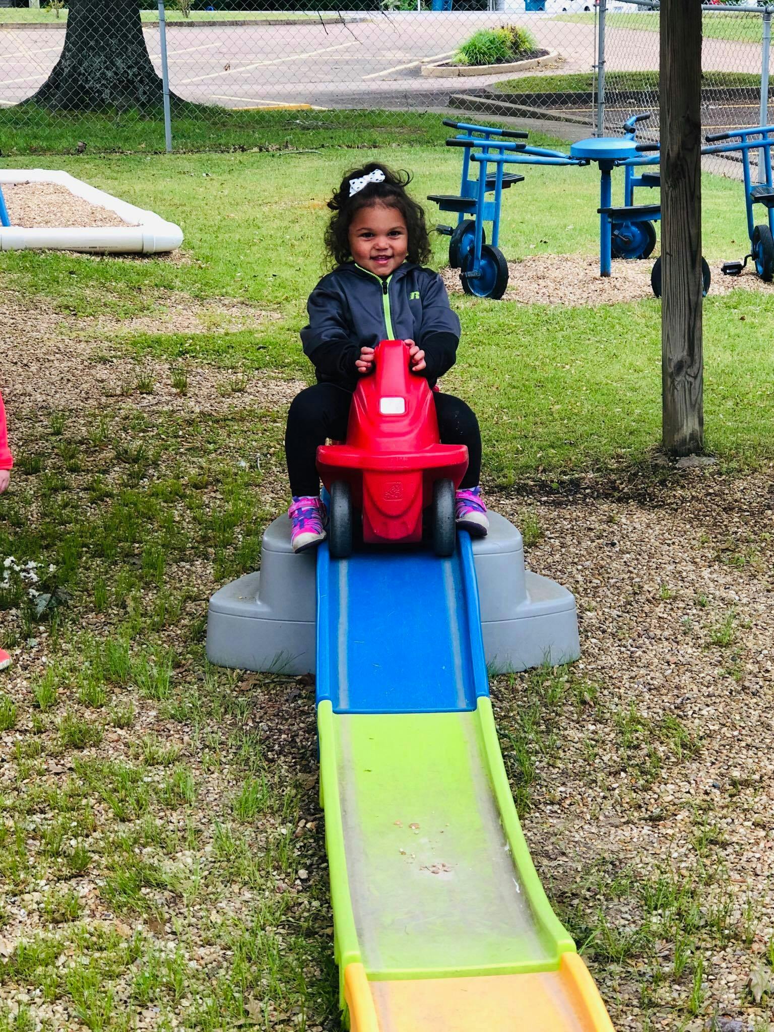 Child on a red toy car at the top of a colorful slide