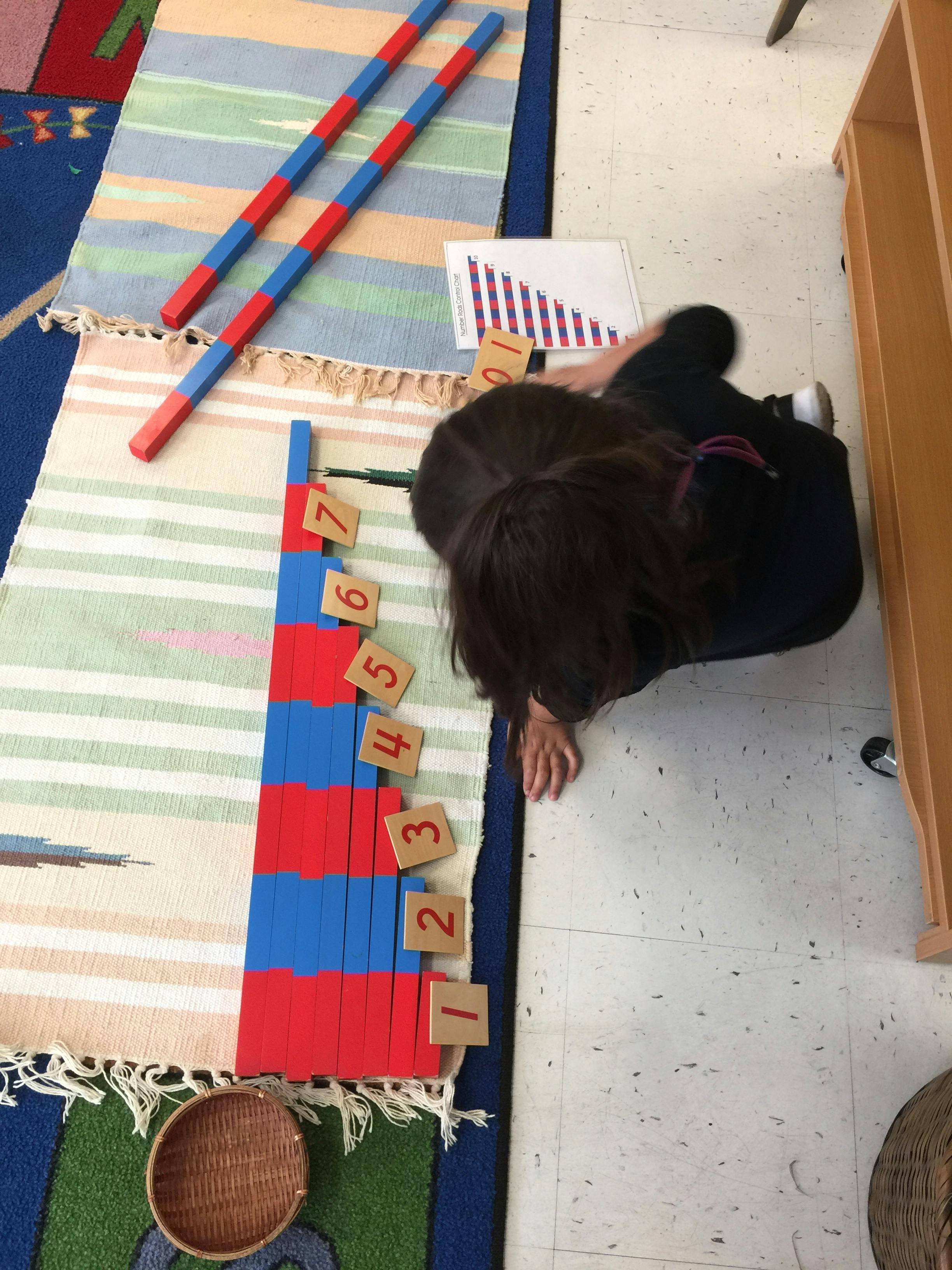 Child on floor with red and blue number rods and number tiles