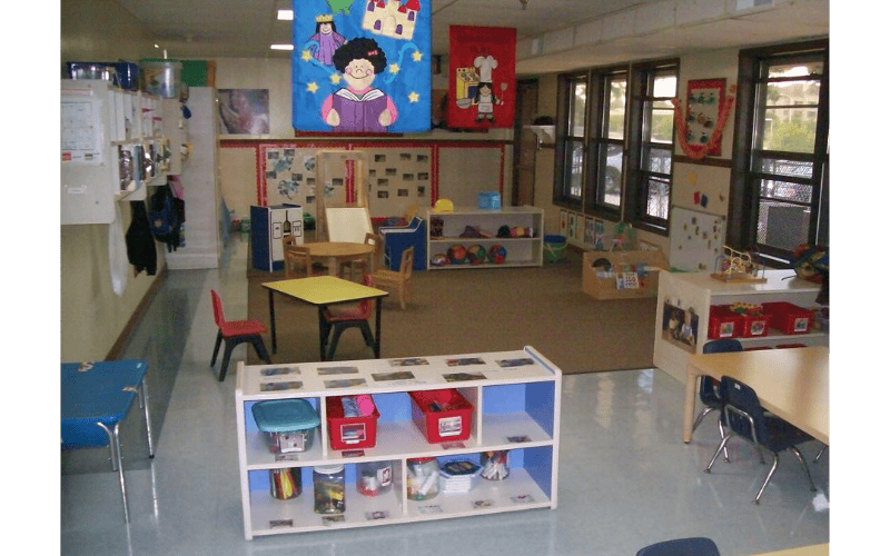 Empty classroom with small tables, chairs, and shelves of toys and books