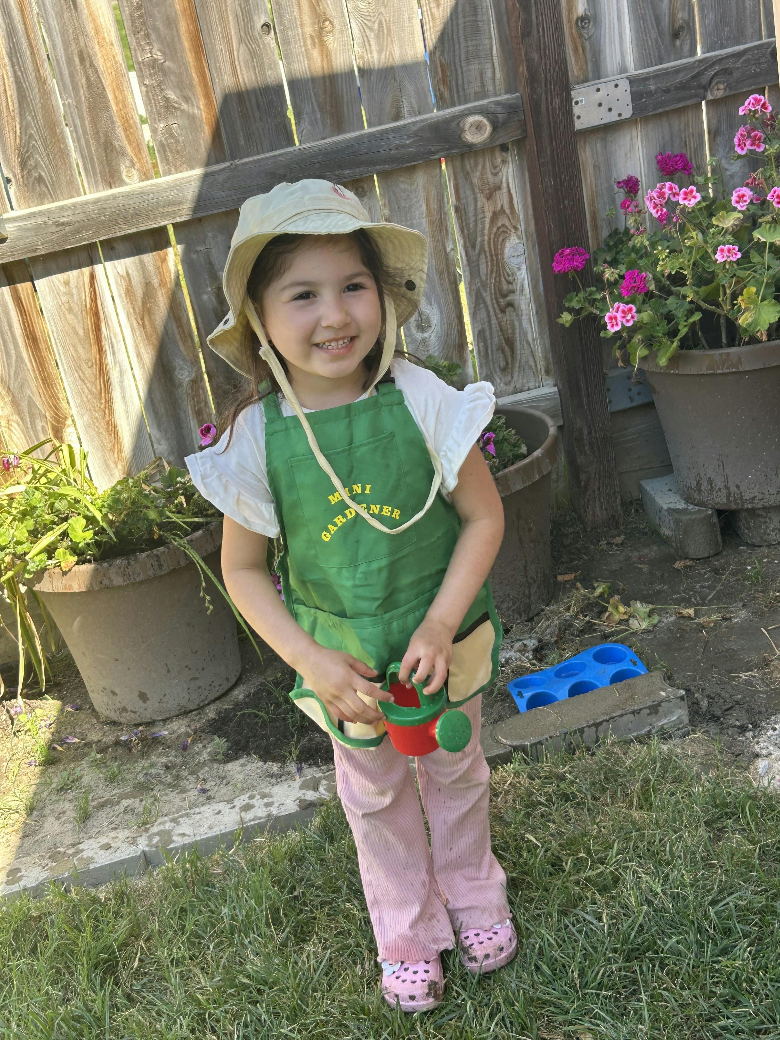 Child in a "Mini Gardener" apron holding a watering can