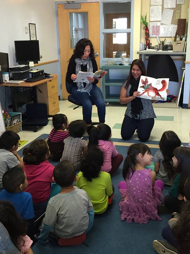 Two people reading to a group of children sitting on the floor