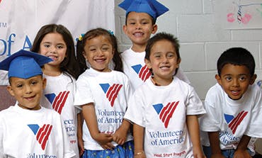 Six children in white shirts, some wearing blue graduation caps