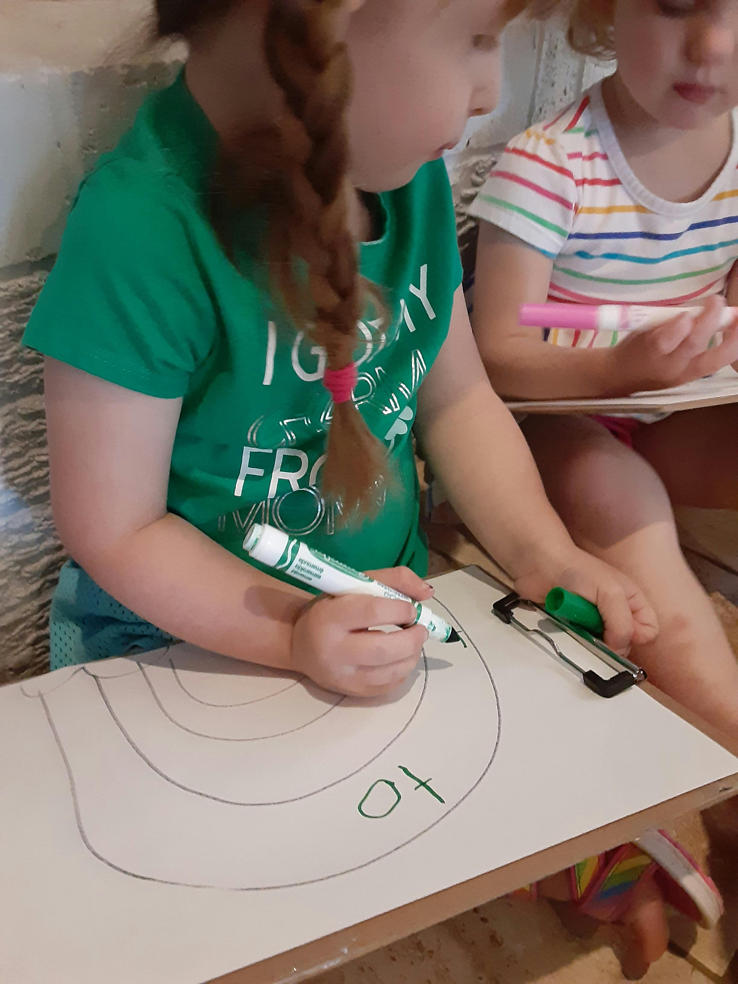 Child drawing on a clipboard with a green marker