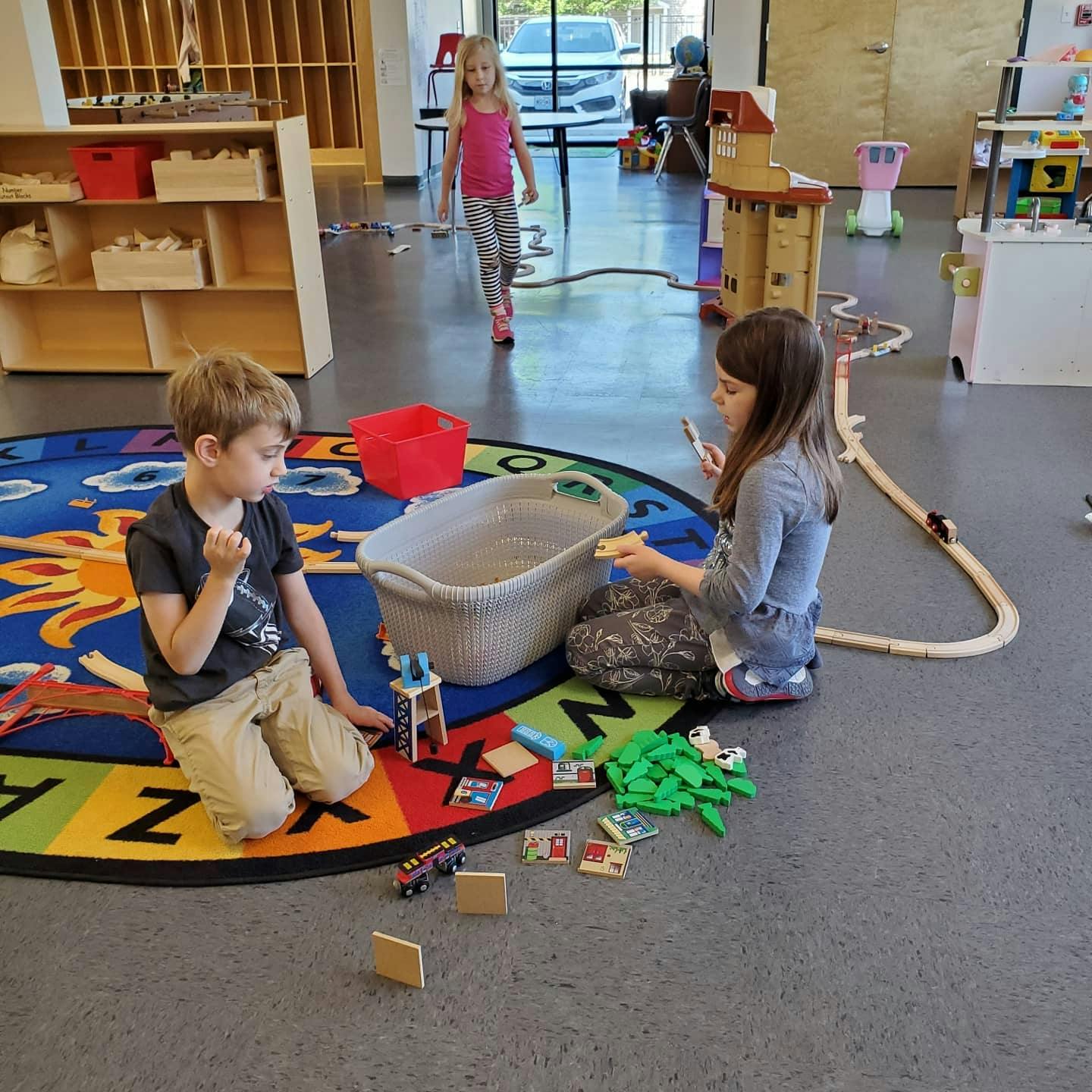 Children playing with toys on a colorful alphabet rug in a classroom