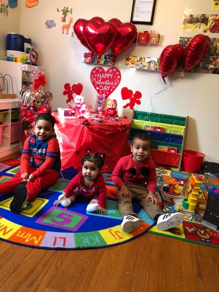 Three children sitting on a colorful rug in a room decorated with Valentine's Day balloons