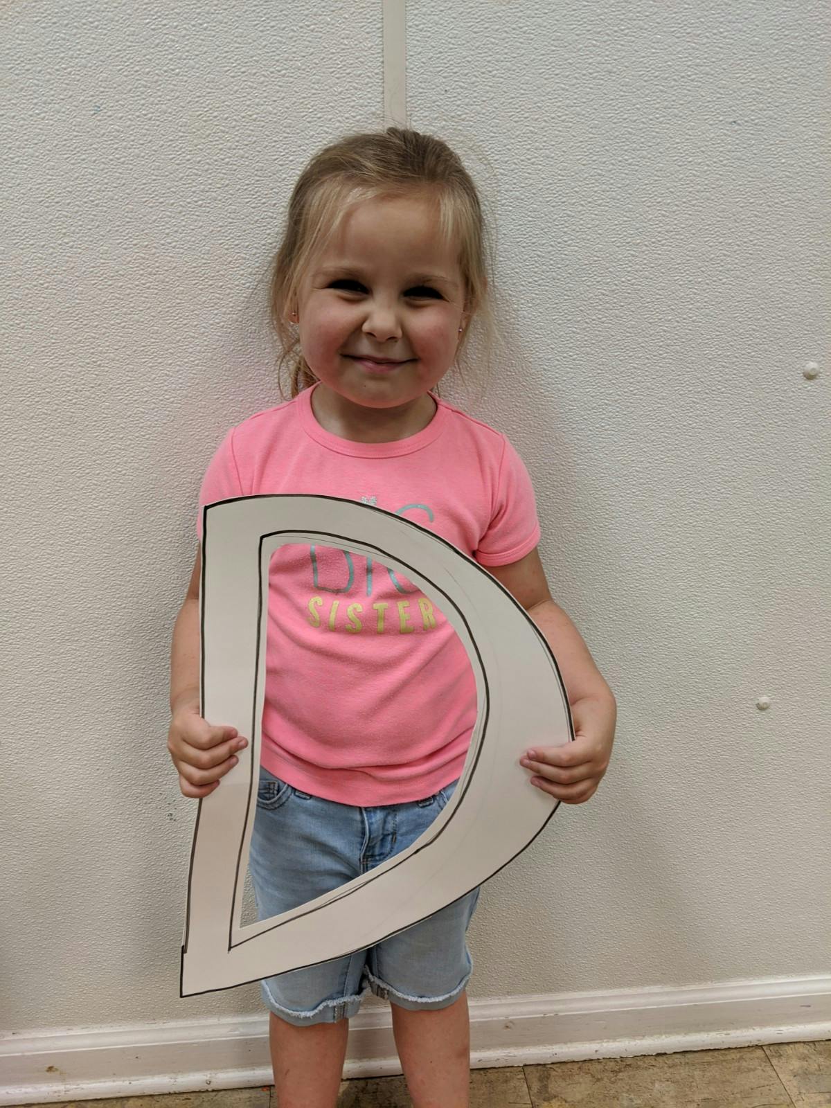 Child holding a large letter D cutout