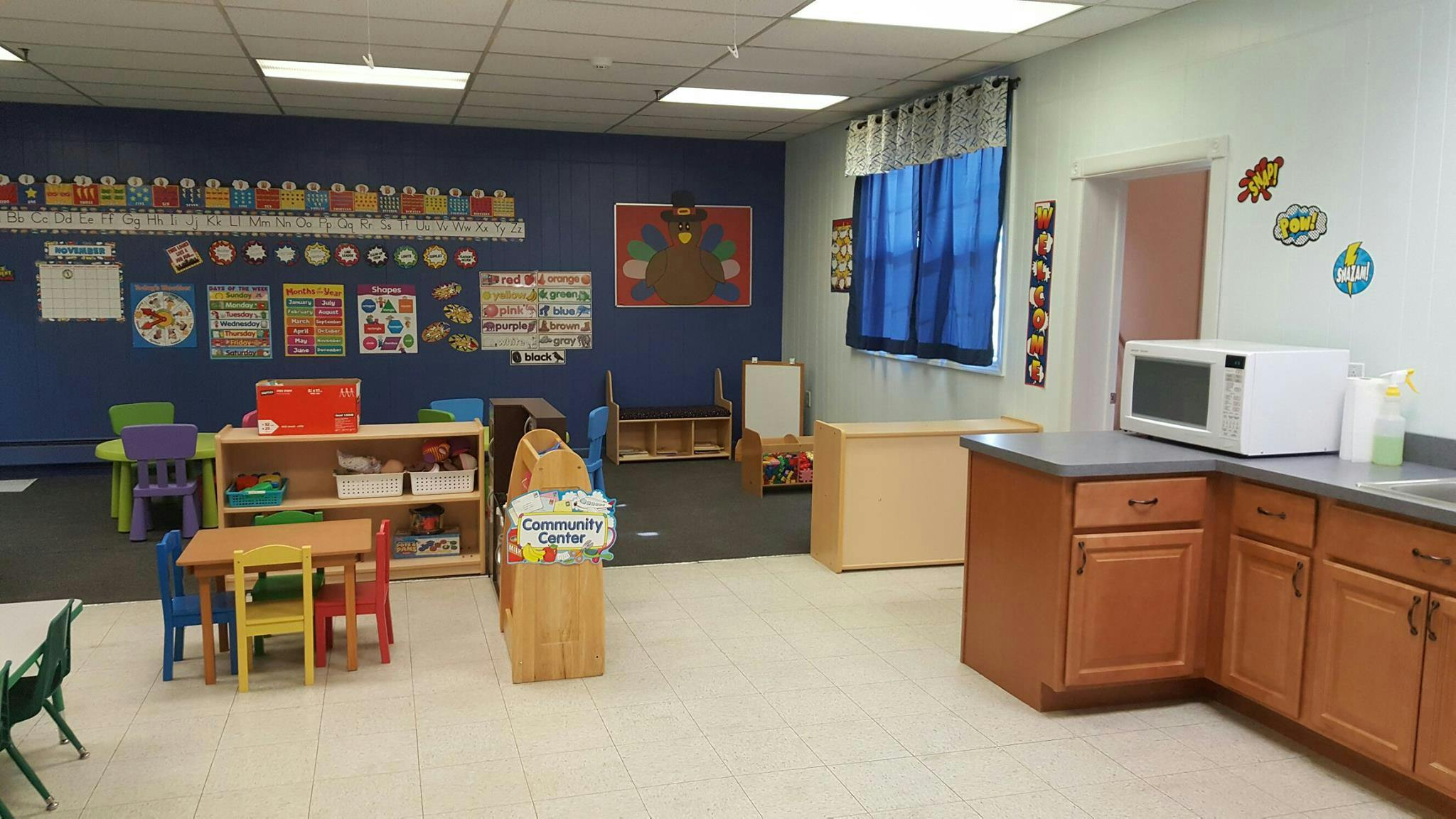 Classroom with small tables and chairs, and a counter with a microwave