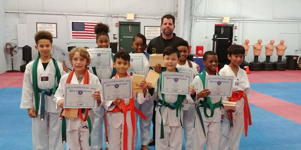 Group of children and an adult holding certificates in a martial arts studio