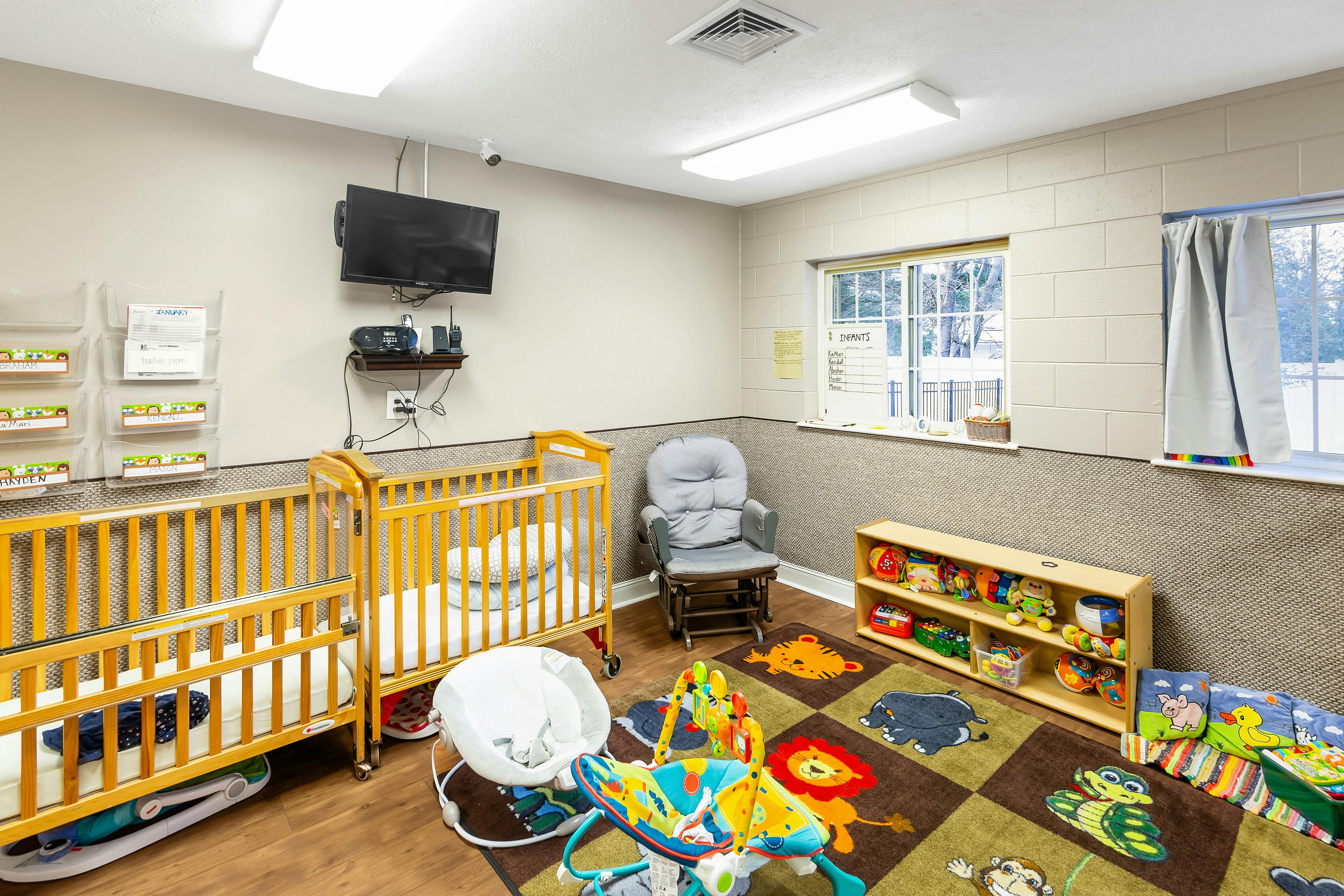 A colorful infant room with two cribs, a rocking chair, and a rug with animal squares