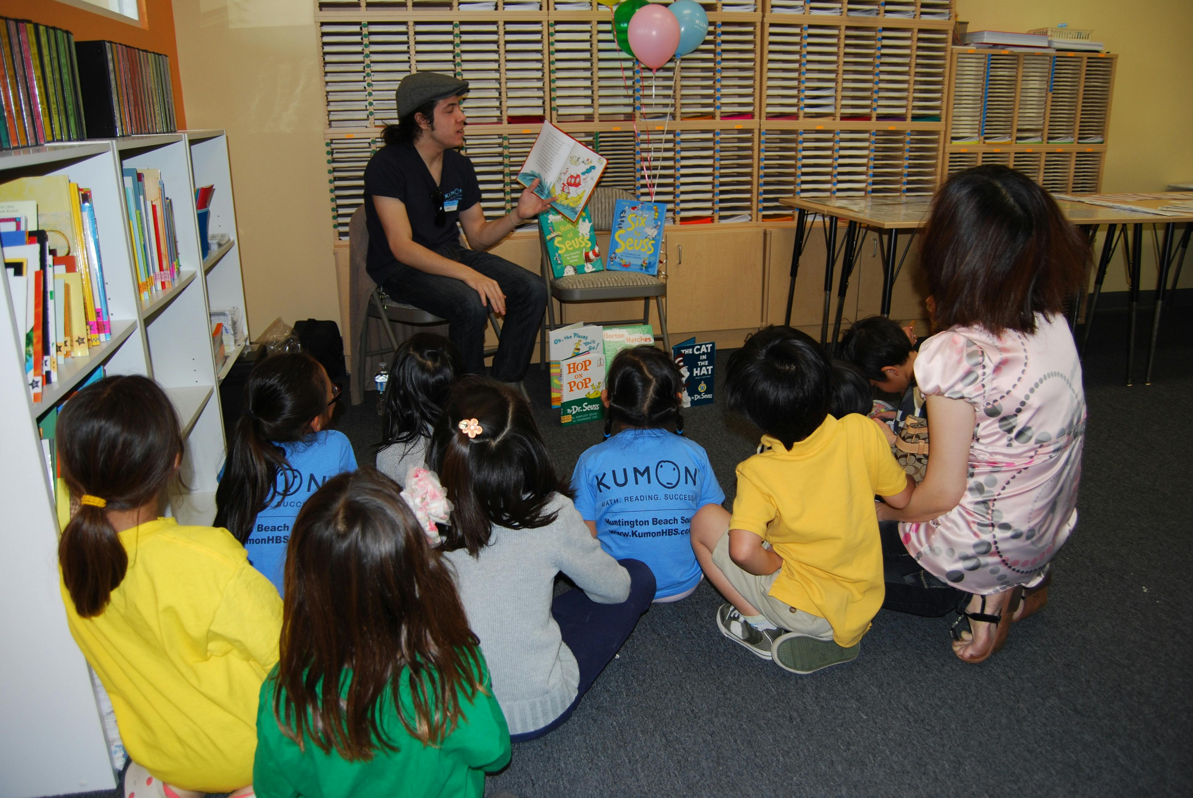 Person reading aloud to a group of children and a person in a classroom