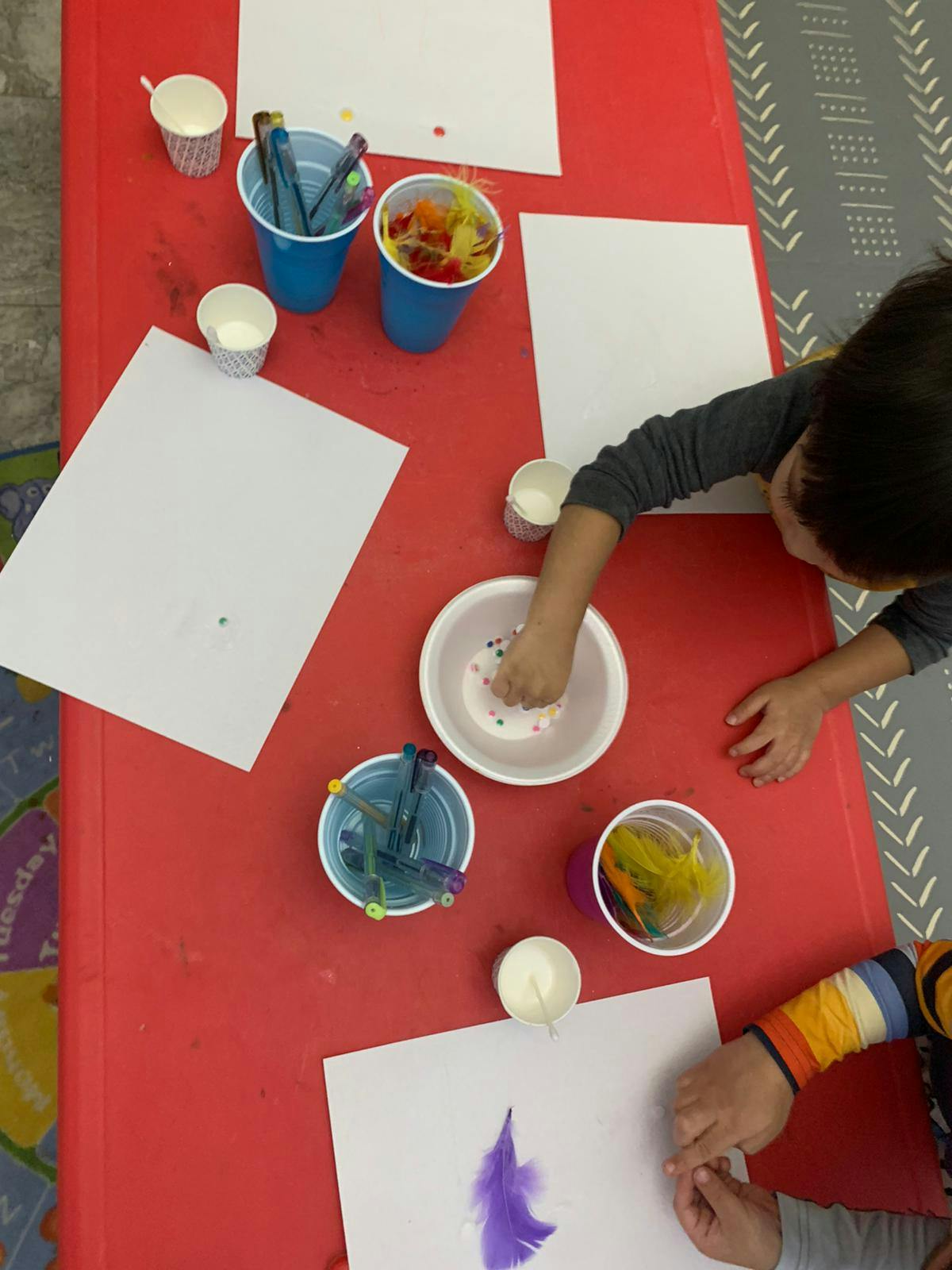 Child's hands reaching into a bowl of small objects on a red table