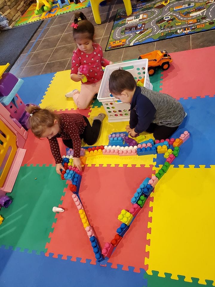 Three children playing with building blocks on a colorful mat