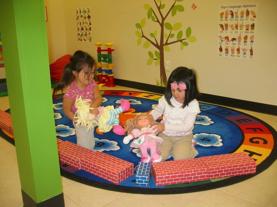 Two children playing with dolls on a rug in a classroom