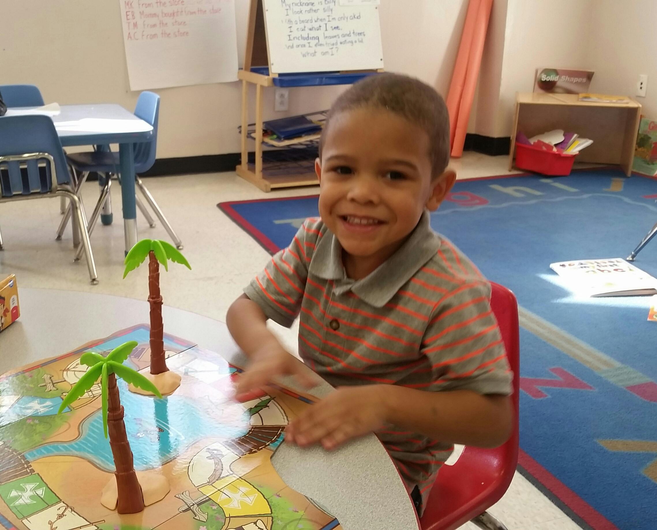 Child sitting at a table with toy palm trees in a classroom