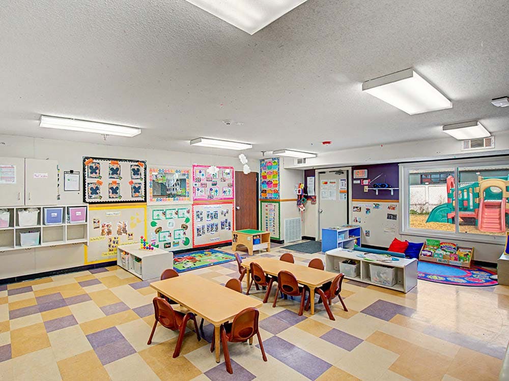 Empty classroom with small tables and chairs, and a window looking out to a playground