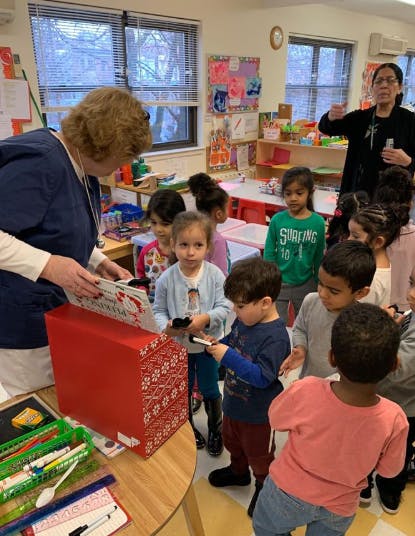 Adult and children gathered around a red box in a classroom
