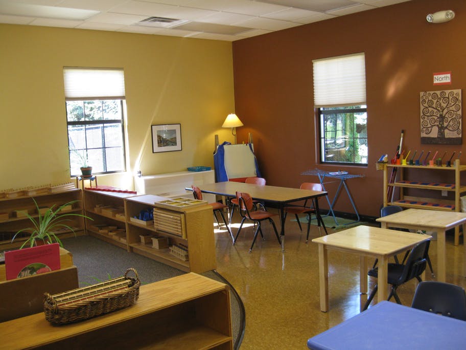 Classroom with small tables and chairs, shelves with learning materials