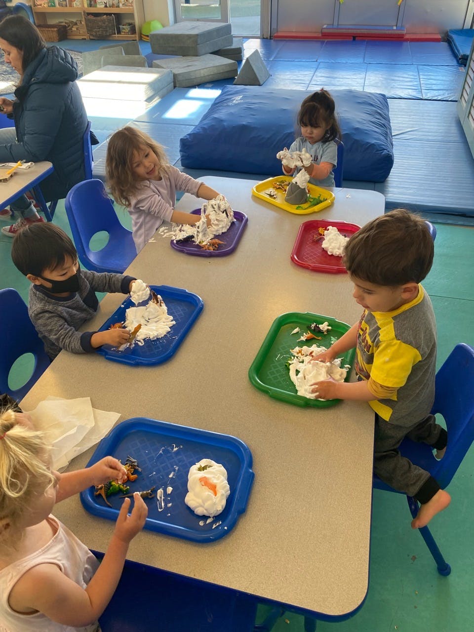 Children playing with shaving cream and small toys at a table