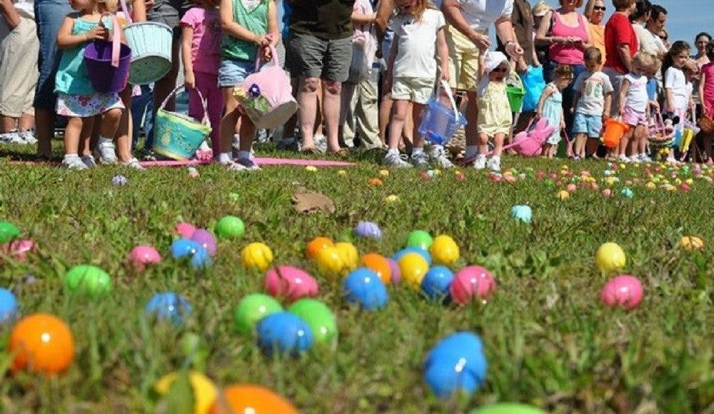 People and children standing in a field with colorful eggs on the ground