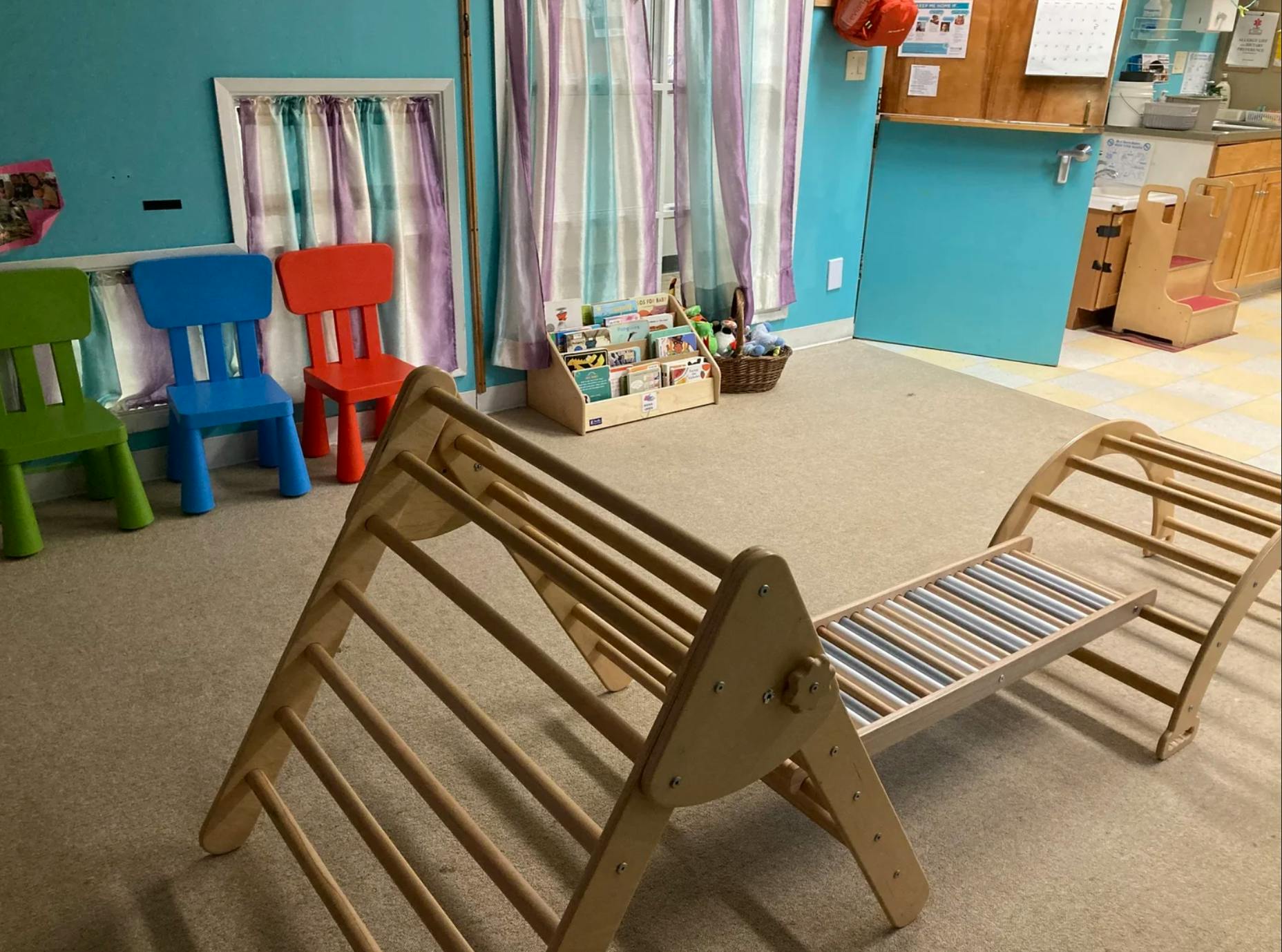 Wooden climbing frame in a preschool room with small chairs and book display
